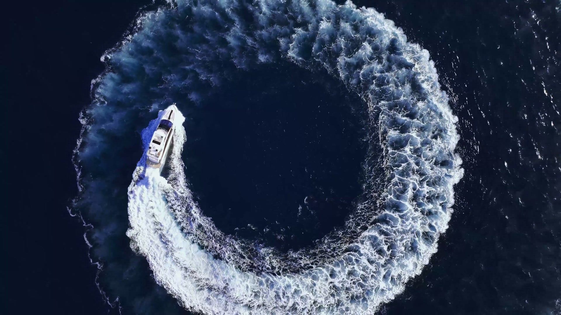 Aerial view of a yacht carving a full white circle in deep blue ocean